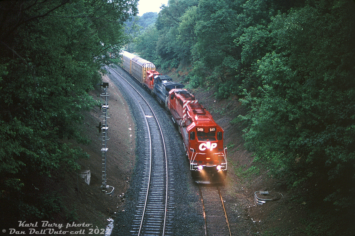 The ditch lights of newly rebuilt CP SD40M-2 5491 cut through the rain as it leads an SD40-2, a Conrail GE and a rebuilt GP9u on freight #526 north on the Hamilton Sub, coming around the curve at Main Street near Aberdeen Yard in Hamilton.

More set in expanding their fleet with secondhand SD40-2's and not impressed by new SD50's or SD60's, CP briefly looked to the rebuild market in the early-mid 90's as a way to acquire more power. Around this time, other railroads like SP and MARC were turning to locomotive rebuilders like MK to satisfy their motive power needs in an economical or specific way that the large builders weren't able or willing to. MK was "building" a large 133-unit order of SD40M-2's for SP using old cast-off SD40 and SD45 locomotive cores acquired secondhand through other railroads, lease fleets, backshop deadlines, etc, and CP decided to place a sample order of 10 SD40M-2 units in 1995. Basically, MK took an old SD40 or SD45 and rebuilt it to SD40-2 standards, complete with either replacing or cutting down the V20 engine blocks in the SD45's into 16-cylinder 645's. The CP units were a mix of SD40 and SD45's originating from a handful of different railroads (SP, UP, C&O, D&RGW), with 5491 originally being built as UP SD40 3022. This experiment was brief and did not result in any follow up orders, as later that year the first of CP's new GE AC4400CW's arrived, and the rest was history. The SD40M-2 units fared as well as the rest of CP's SD40-2 fleet, and at one point some found themselves in yard service in Thunder Bay and Calgary.

Karl Bury photo, Dan Dell'Unto collection slide.
