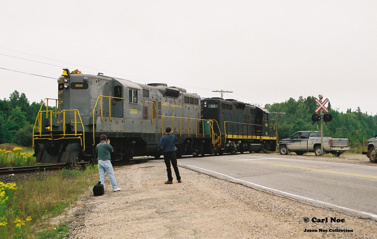 In 1996, CN had officially abandoned their Newmarket Subdivision between Barrie and Longford Mills, severing the mainline as a through route and putting the Canadian on the preferred Bala Subdivision route permanently.  While this section of the line had received extensive attention during its final runs, CN had also deemed the northern section of its Newmarket Subdivision between North Bay and Capreol as no longer required as the only freight traffic on this portion would have been occasional run through trains using the subdivision to reach Capreol. And with trains 450/451 only operating between Toronto and North Bay it was put up for discontinuance. Following its approval of abandonment, CN had contracted emerging company Cando Contracting to remove the heavy mainline rail for them. In the days before internet, cell phones and social media this lengthy operation basically went on virtually undetected and photos are very scarce despite the fact this was still an active mainline until the end. A lot of this had likely to do with the majority of this line being very remote and photo locations not very accessible. 

So then this is where the expect the unexpected part of the hobby comes into play during one of yearly northern Ontario railfan trips. 

In late summer 1997, a group of us were heading to Sudbury and decided to detour through North Bay during the morning, hoping to catch something on the Ottawa Valley Railway along the way. That morning, it was very foggy and after some photos at the CP North Bay station we continued our journey on the Trans-Canada Highway towards Sudbury. I believe some of us were even beginning to start nodding-off when a friend suddenly said “Ah buddy there’s GP9’s over there!”  Yup there sure was. Catching us totally off guard were Cando Contracting 1000 and 94 as they slowly appeared between trees , headed to their waiting rail train that was likely situated somewhere in the remote wilderness. At this point the line started paralleling the highway from North Bay within sight so we were able to get ahead of the units and quickly pulled over at the crossing where the Trans-Canada highway intersected it. A mad scramble ensued as camera bags were quickly opened and we all piled out of my dad’s van as we set-up to photographs the units going over the highway. The crossing protection had been previously disconnected so Cando workers had to protect the movement each time a train crossed it. Unfortunately, myself and a friend got in my dad’s photo of the units as they crossed and he likely got one of the best photos of all of us as seen here. The late 90’s were crazy times; where high-hood GP9’s could tear out a mainline virtually unnoticed and then go on to start second careers on  new shortlines the following year.