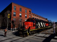 A pair of GP9's are returning to the main line after dropping off grain cars at Ardent Mills. They are crossing Charlevoix Street and a crewmember is flagging.