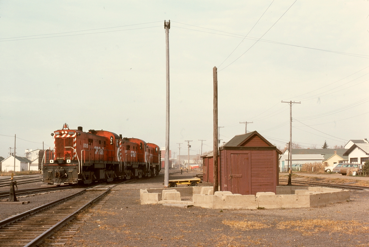 At Prince Albert in 1976, clear evidence of steam days remained as the foundation for the water tower stood firmly in the CP yard, with a trio of RS-23s, 8015+8017+8018, passing by on Wednesday 1976-09-29, preparing to take a train to Meadow Lake.