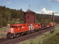 Westward trains between Princeton and Merritt were at night for many years during high tonnage operation, but as traffic declined, operations were reorganized and provided daylight opportunities, allowing this Tuesday 1984-06-19 view at the Brookmere water tower of two GP38ACs where quartets of them had been common in days with heavier trains.  Above the cab of 3001, note the roof of the relocated depot, previously situated about alongside the first carload of lumber.  Since that photo, rails have been removed (1989) in favour of a rail trail, the depot was destroyed by fire, and the two-spouted water tower was relocated northward about 20 metres to GPS 49.81810, -120.87199.

<p>Both locomotives survive today at 52 years since built, 3001 as maintenance of way power unit CP 403011, and 3002 as a regular roadswitcher.