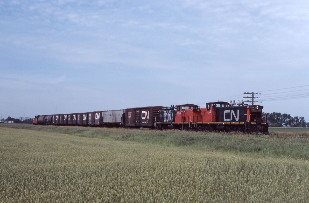 GMD-1s 1008 and 1050 lead an eastbound away from Portage la Prairie and towards Winnipeg's Symington Yard. By this time, branch lines requiring light weight power were becoming fewer and fewer as the Prairie Branch Line Rehabilitation Program (implementing the recommendations of the 1977 Hall Commission on Grain Handling and Transportation for branch line rationalization) was well under way. In a few days, on August 1st, the Western Grain Transportation Act will take effect, effectively abolishing "the Crow" rate and ramping up changes to the handling of Canadian grain. At the time of the photo, CN had already converted 12 GMD-1s to B-B trucks and would eventually convert 46 of 83 A1a-A1A units (including the 1050 and former NAR GMD-1s) to that configuration. Lead unit 1008 would be re-manufactured as the 1602 in 1988 and re-trucked to B-B unit 1432 in 1999.