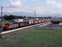 August the 1st, beginning of a new crop year...and both CN and CP are moving grain empties west for reloading. In the foreground, a pair of SD40s (5168 and 5172) have a colourful consist of government-owned cover hoppers in tow as they approach West Tower where CN's Rivers and Gladstone subs cross the CP Carberry sub 0.8 miles to the west. In the background, a similar CP train behind SD40-2 5723 and GP35 5021 waits its turn at the diamond. (Photo taken from the Provincial Road 240 bridge.)