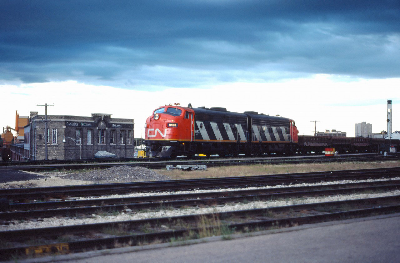 Normally assigned to passenger trains to Thompson and/or Churchill, today two of the F7Au locomotives based in Winnipeg have drawn a work train assignment, probably for the Prairie Branchline Rehabilitation program that was going on at the time (note the side-dump cars). On their way back to Symington, these units are passing the VIA station and CN's Prairie Region offices. In the background, you can see buildings from the East Yard which at one time hosted extensive team track and express facilities and still had VIA's coach in the early 1980s. Today, the area east of the Station is The Forks market.