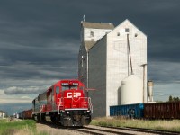 Spotless CP 5989 leads work train E07 past the old elevator at Southey Saskatchewan under threatening skies.  E07's task for the day was lifting and setting out loaded and empty tie gons at various points along the Bulyea sub as part of a large tie replacement project in the area. 