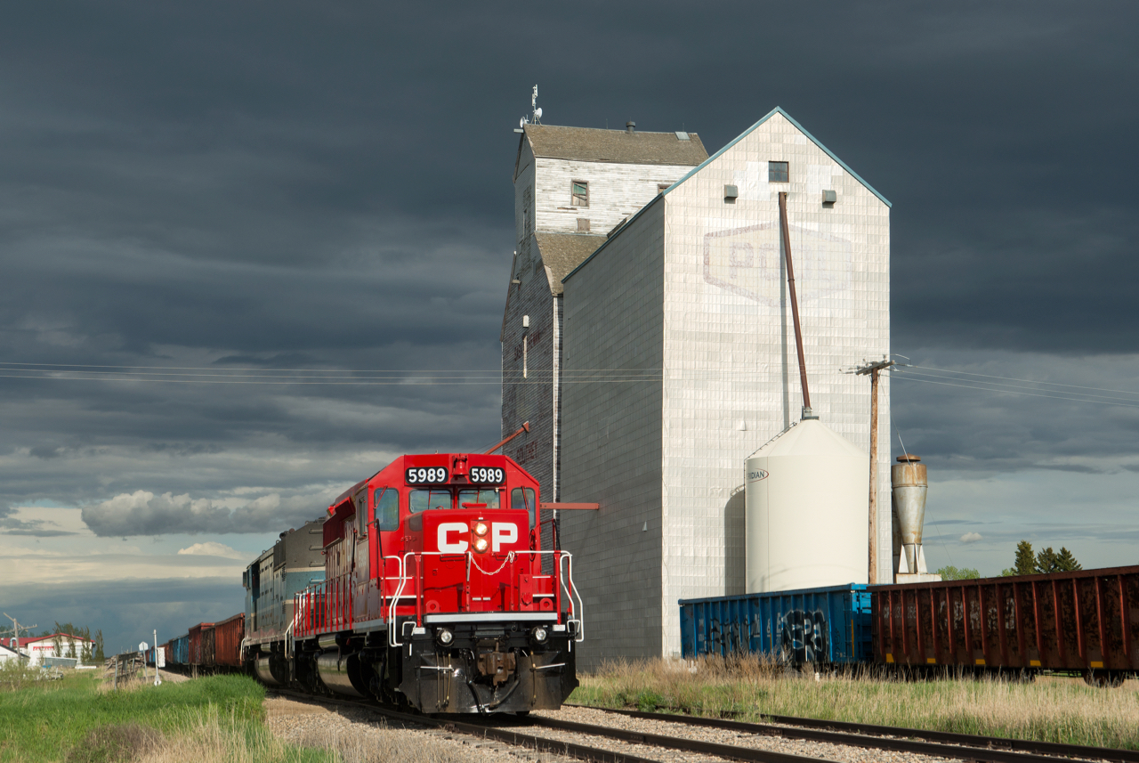 Spotless CP 5989 leads work train E07 past the old elevator at Southey Saskatchewan under threatening skies.  E07's task for the day was lifting and setting out loaded and empty tie gons at various points along the Bulyea sub as part of a large tie replacement project in the area.