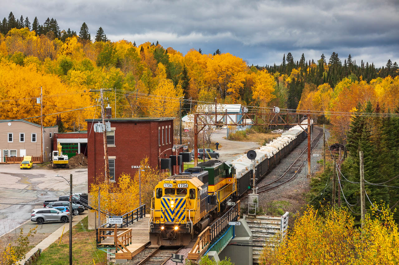 Under brooding autumn skies — that, in retrospect, may have been foreshadowing what was to come — a pair of Ontario Northland EMD SD40-2s hustle Timmins to Englehart train no. 308 past the line-side sentinels at Swastika, Ontario. 

Unbeknownst to the photographer, less than 6 months after this photo was taken, the unique 1967-constructed station and surrounding signals would be reduced to a heap of rubble. 

With the demolition of the town's station, Swastika not only lost a piece of its railroading heritage but a sense of character. All too often, the railroad landscape of today seems to become more and more sterile as the aesthetic of place is drowned out by ubiquity. An unexpected demolition such as this illustrates the point and serves as a reminder that in railroading, the only constant is change.