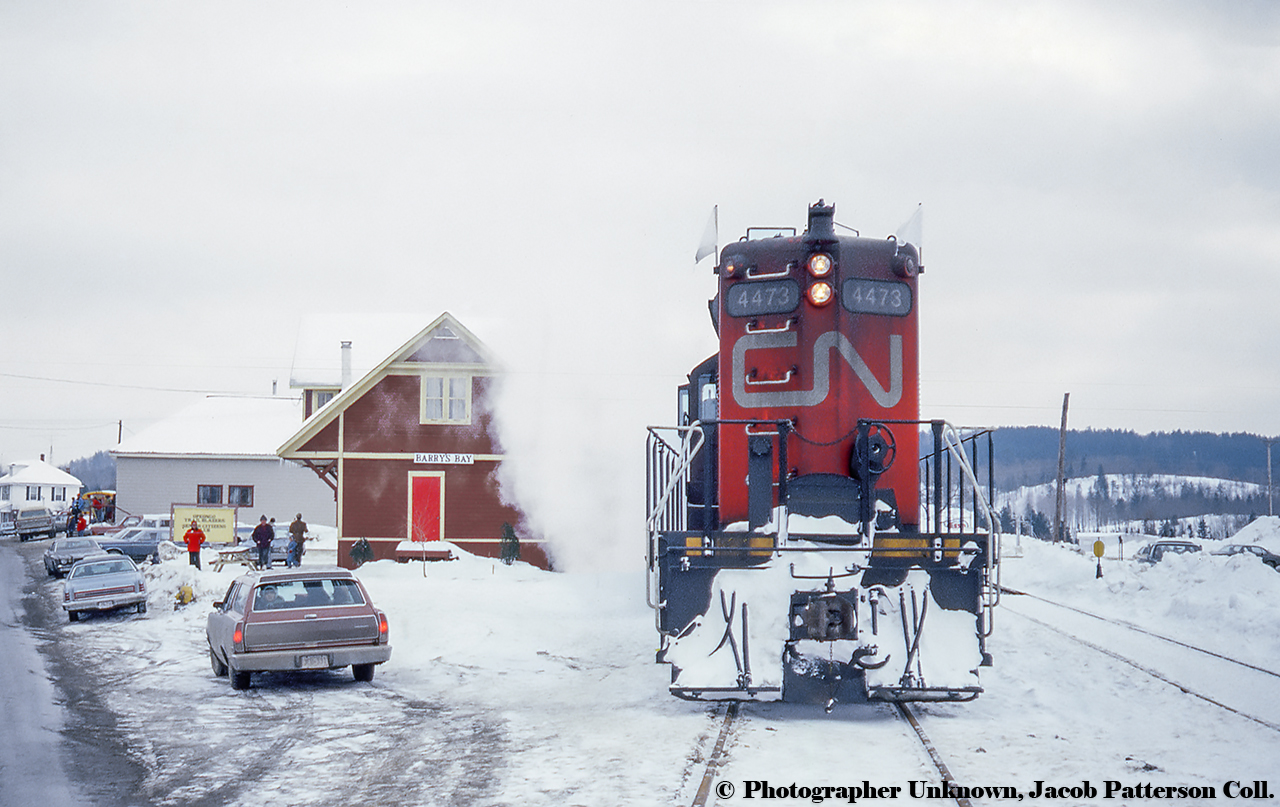 The weekend of February 18 & 19, 1978 saw Barry's Bay busy with activity as the ski train, running for it's second of three weekends, arrives from Ottawa with folks ready to hit the slopes at Mount Madawaska, and take part in Timberfest '78, Barry's Bay's logging themed winter carnival.  Per articles from the Ottawa Citizen (page 121, thanks to Colin Churcher,) the trains were spearheaded by Dick Howey (Nepean-Aylmer Transit Committee) to raise funds for the Nepean senior citizens.  Costing $35,000 for the four weekends, and funded by provincial and federal grants, plus funds from various local organizations, there was originally four scheduled weekends, however poor sales cancelled the first trips on February 4/5.  the following three weekends, trains departed Ottawa at 0730h, arriving Barry's Bay about 1215h with stops between at Bells Corners and Renfrew.  The return trip would depart Barry's Bay at 1800h, arriving Ottawa about 2230h.  As seen on the sign in front of the old station, the building is in use by the Opeongo Trail Blazer's Club who took us residence in the building in 1974, over a decade after the CNR ceased passenger service on June 30, 1961.  The group, since renamed Opeongo Senior's Centre, moved into a new site in 1991, and the station building survives today as a tourist information centre.Little traffic operated over the Renfrew Sub by this time.  The line west of Barry's Bay to Whitney saw it's last train in 1974 and had suffered washouts in the following years.  The January 7, 1982 announcement in the Eganville Leader cut direct service in half with a winter line closure west of Renfrew, trucking available from Pembroke.  Regular service was terminate in January 1982, and abandonment was formally announced in the Ottawa Citizen on August 8, 1983.  Rails would be removed not long before Steve Danko's 1986 shot.  Nearby, Barry's Bay has also preserved the old wooden water tower.Original Photographer Unknown, Jacob Patterson Collection Slide.
