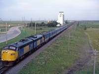 Ten miles to go! VIA train No. 92 is about to cross under the Perimeter Highway as it enters the City of Winnipeg, passing the elevator which was located at mile 10.9 of the Rivers sub. After years of running with CN F7Au locomotives, VIA stopped using leased CN engines on this train and replaced them with remanufactured FP9ARM units in the spring of 1984.Units 6300-6304 were not equipped with steam generators, lightening them to 247,000 lbs (rather than the 260,000 lbs of units 6305-6314). VIA 6302 (former VIA/CN 6533) and 6304 (ex-6509) are "back-to-back", unlike later years when the units ran "elephant style".