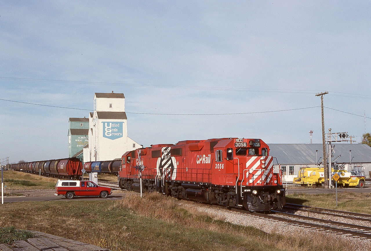 On the Lacombe sub. in central Alberta, an eastward Coronation Turn with a pair of GP38-2s, 3056+3130, is returning to their train of empty grain hoppers after spotting empties on the elevator track.  Nowadays the rails only reach 15 miles to the west at Botha.