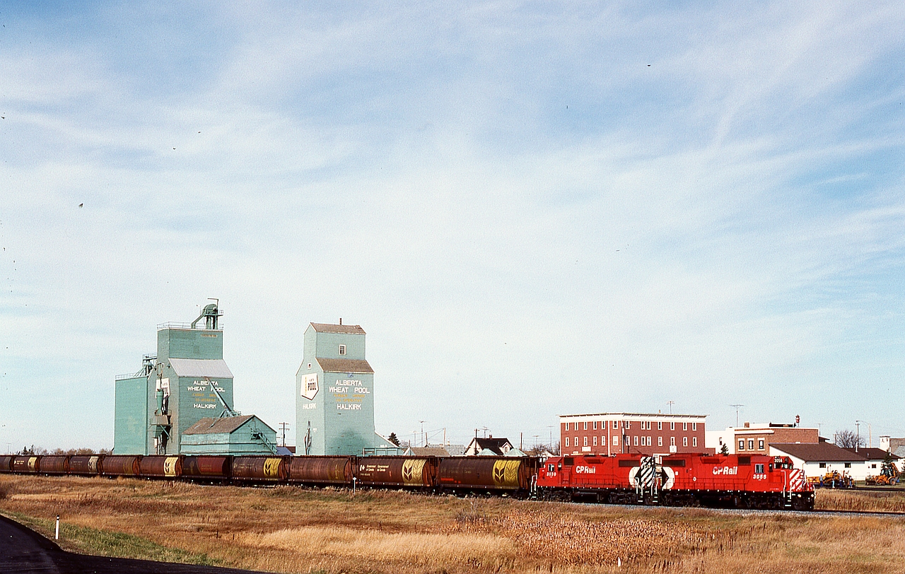 On the CP Lacombe sub. in central Alberta, a Coronation Turn with a pair of GP38-2s, 3056+3130, is eastward at 1117 MDT on Sunday 1991-10-06 with twelve empty grain hoppers through the village of Halkirk at mileage 33.7.  Nowadays the rails only reach 15 miles to the west at Botha.

Yes, this is the same train as posted last week, that one originally marked as at Halkirk but with the wrong photo, and actually at Stettler, as first noted by SD70Dude.  Thanks to Steve Host for straightening that entry out for me.