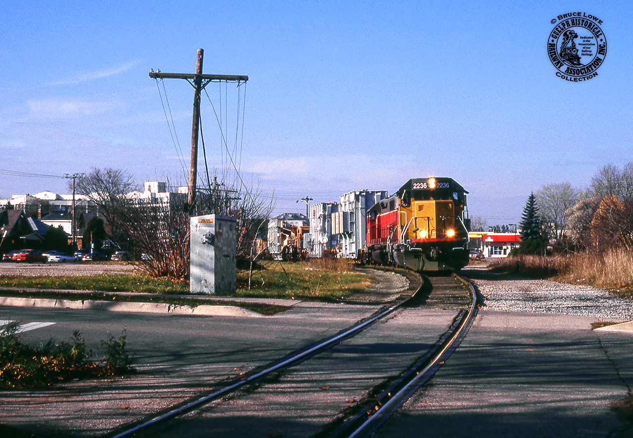 A dimensional movement of three transformers from ABB, two on flatcars, the third on schnabel car HEPX 200, crawl slowly through Guelph approaching Suffolk Street.  The site seen here used to have much more rail activity with the Guelph City Spur branching off towards the pine tree, customer Federal Wire & Cable Co, later Pirelli Cable off to the right, and an interchange connection with the Guelph Radial Railway at right on Suffolk Street before it was removed in 1929.  The Pirelli site is now a housing development, their parking area at left is now a park, and the City Spur was pulled up in 1972.