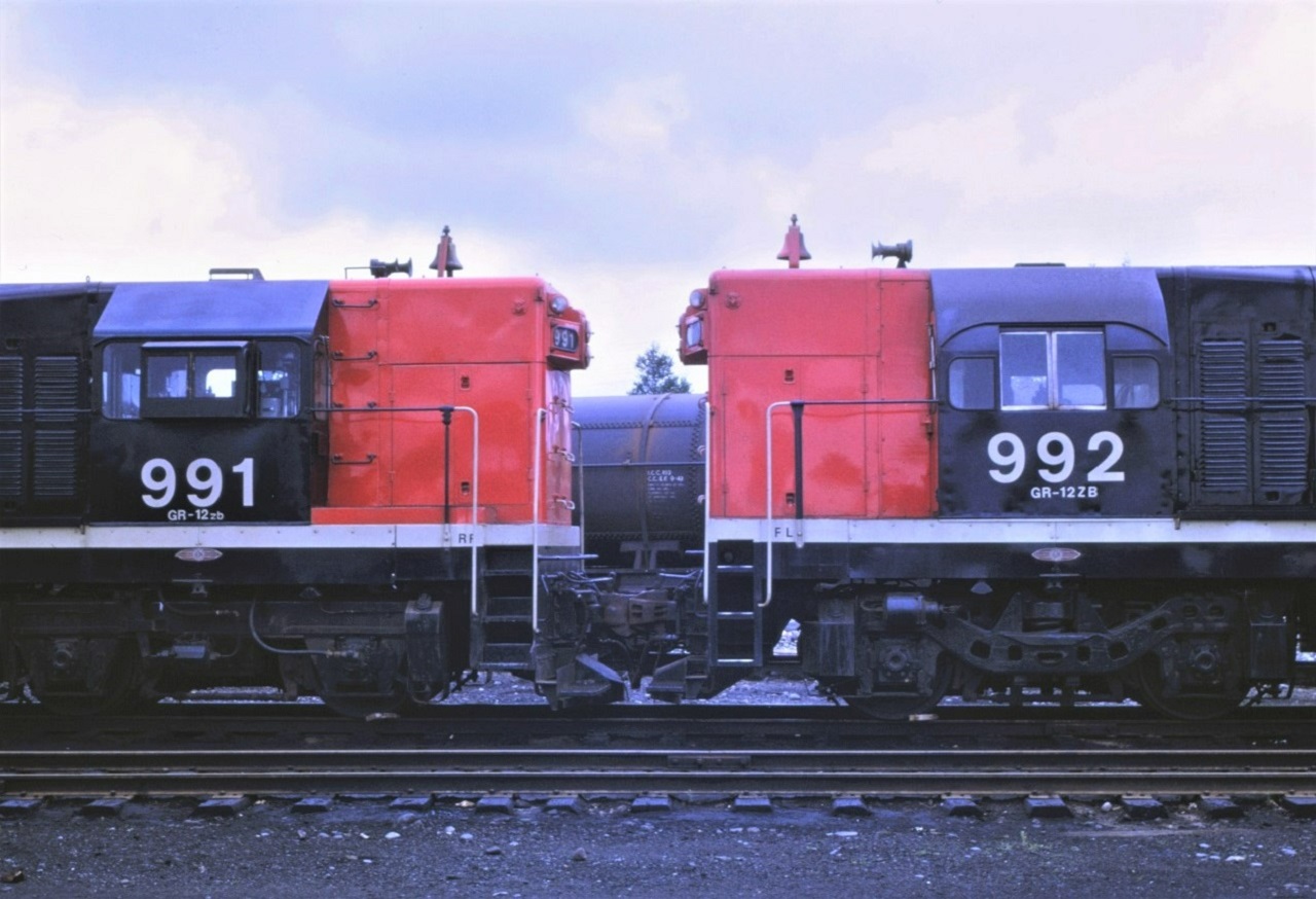 Just passing through!!!  CN's two G-12s, 991 and 992, are shown in Capreol, Ontario on their way west to their new home on Vancouver Island.  The units were built for the London and Port Stanley Railroad in 1955 and 1957.  991 ex L&PS L4 built 8/1955 b/n A832 (some sources show the b/n as A831) and 992 ex L&PS L5 built 7/1957 b/n A1324.  Both units acquired by CN on January 1,1966 and retired in 1976 and scrapped. Of note are the different trucks and cabs on the units.