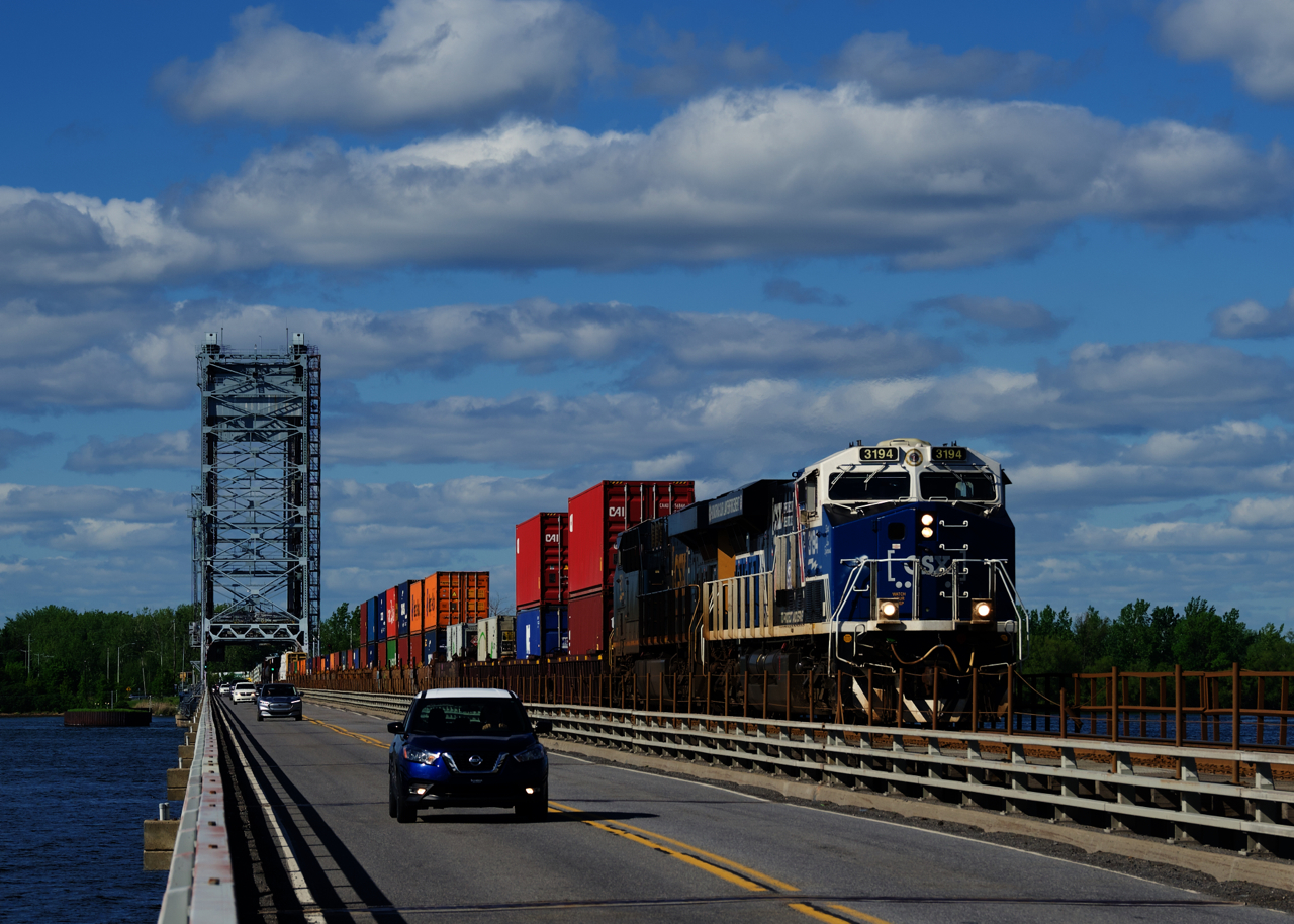 CN 327 with CSXT 3194 in the lead (with its white and blue nose) is being passed by a blue and white Nissan as both cross the Beauharnois canal on the Larocque Bridge.