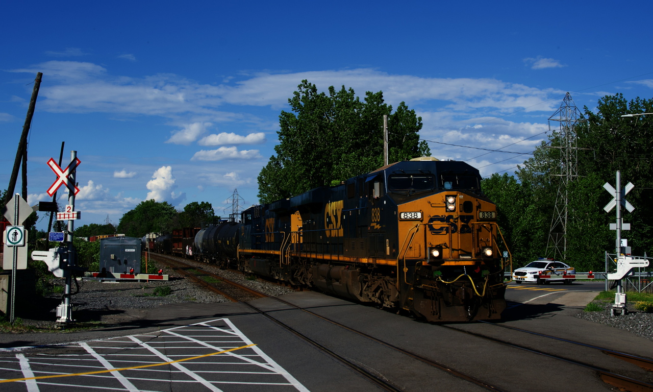 A 272-axle long CN 327 has CSXT 838 & CSXT 7016 for power as a police car waits at a crossing.