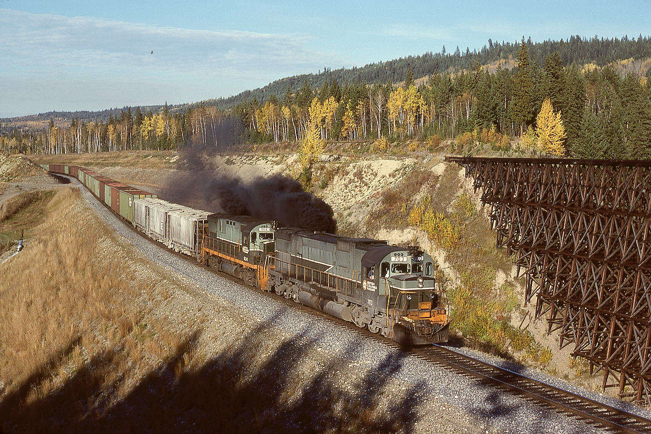 At Australian Creek at mileage 364.3 and between Kersley and Alexandria, the British Columbia Railway bypassed their maintenance-intensive timber trestle with a fill and a culvert, creating a notable dip in the track profile.  Train number 34 from Prince George on Thursday 1978-10-05 had all-MLW/ALCo power, 703+804 on the headend and remotes 730+702+RCC1, and is seen here notching-out at the bottom of the dip at 1631 PDT.
