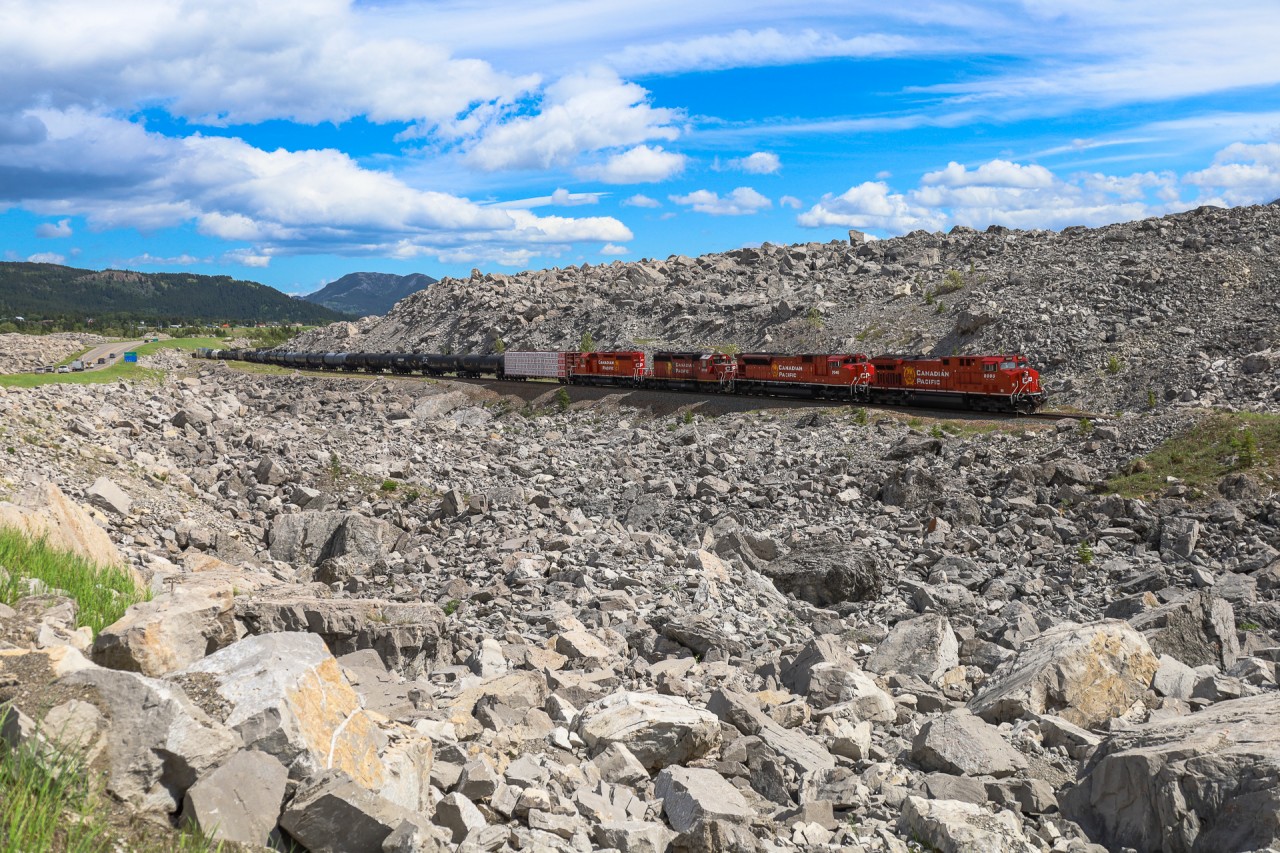 This has to be one of the most awe-inspiring places that I have ever been.  I had heard of Frank Slide before and seen photos, but I did not imagine the devastation was as wide spread as it was and that the rocks extended this far into the valley.  The place is surreal.  Just a short walk from the highway and you'll see anything from massive boulders, to tiny stones and pieces coal scattered around.  It is definitely worth the visit.  119 years after the devastating slide, we see CP 219 with CP 8000, CP 7046, CP 5792 and CP 5973, with CN 3905 on the tailend, climbing through the debris field at Frank Slide.  

In the early morning hours of April 29, 1903 the peaceful mountain town of Frank, Alberta was awakened by the thunderous sound of a rock slide on Turtle Mountain.  Within 100 seconds, 110 million tons of rock fell into the valley below at speeds approaching 70 miles an hour.  When it was all said and done, over 90 people had lost their lives and 3 square kilometers of the valley were buried by rock averaging 46ft deep, with some places being buried 150ft deep.  At the time, this was the largest recorded land slide in Canadian History and the CP mainline was buried for approximately 1.2 miles.  Within 3 weeks the railway had blasted a path through and re-opened the Crowsnest Sub. The eastern end of Frank, Alberta was devastated by the slide and the town was relocated out of the path of Turtle Mountain.  The mountain has since been outfitted with sensors, to monitor it for any signs of movement, as scientists believe it is only a matter of time before Turtle Mountain gives way and another massive landslide affects the valley.