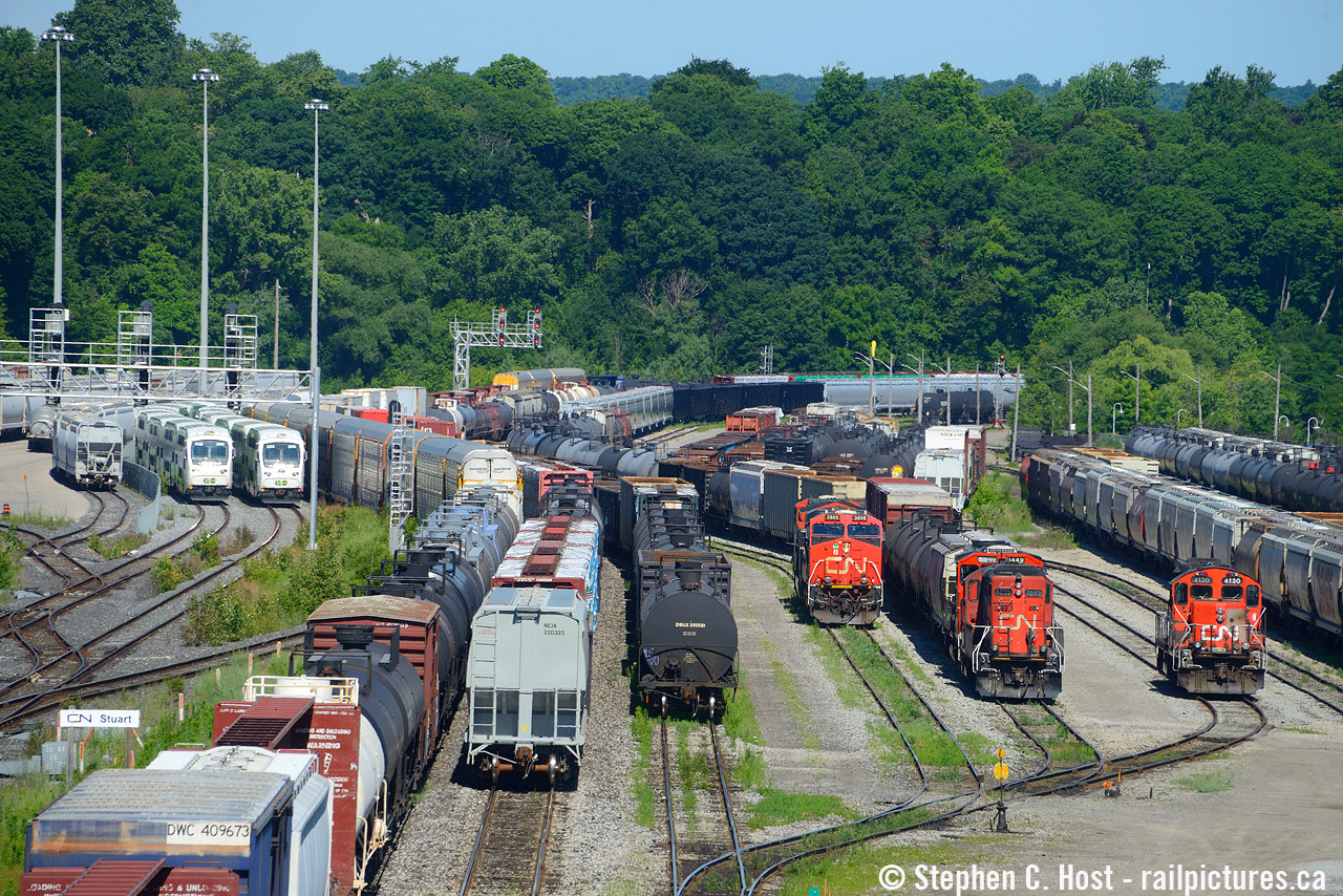 How many trains do you see? A full house at Hamilton due to some unusual circumstances. With CN 421 and 422 BOTH working the yard, the 'hot' track and yard track are both in use in Hamilton. This meant GO trains had to both take the plant at dundurn over to stuart on the newly constructed tracks for West Harbour GO. Two GO trains are pictured at Stuart at the signal bridge - one on the left is sitting waiting at the signals stopped for CN 422 to clear the hot track. The GO train just to the left of it is coming in as it is part of the all-day service to West Harbour and has nothing in the way. Out of sight is the 0800 Hamilton Yard working the east end. You can see three sets of CN power: A GP9 from L351 sitting in the yard, and set of power that the 0800 will have to switch out was set off by 421, and of course, the mainline power is 421 going for their lift in the Hamilton yard. Busy times, but only for brief minutes :)