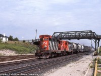 A westbound CN local behind a pair of GP9s, passes through Woodstock beneath the old Bay Street bridge.  The lead unit is equipped for snow plow service with radiator covers atop the long hood.  Both geeps have been rebuilt and are still on the roster as of 2021.  4518 as slug 247, and 4577 as GP9RM 7226.<br><br><i>Original Photographer Unknown, Jacob Patterson Collection Slide.</i>