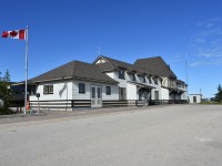 The street address for the Churchill, Manitoba railway station is 1 Mantayo Seepee Meskanow.
Once arriving passengers have detrained and been picked up by their respective lodging shuttles, the onboard crew has finished their arrival chores, and the VIA maintenance personnel have the wayside HEP connected through the lead locomotive, it gets pretty quiet at this location.
For this photo, I am standing in the middle of the street without a vehicle in sight, so my less than stellar photographic skills are not interrupted once during my picture taking time on this particular morning.
The early sunrise and late sunset in Churchill offered lots of opportunity to capture a plethora of views of the station and other interesting sites in town during my three day stay.
The Canadian Government has recognized the station as a "Recognized Federal Heritage Building" since June 2000.