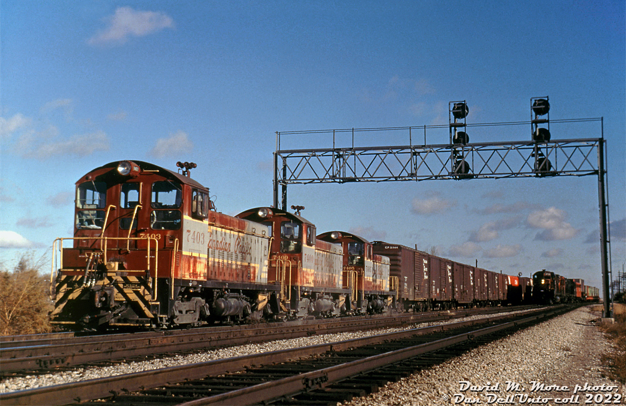 You might have seen this photo in black-and-white before: maybe in the pages of Dean & Hanna's Canadian Pacific Diesel Locomotives book, or maybe on Ray Kennedy's Old Time Trains page on Toronto Yard.

Three of CP's six GMD SW9 switchers, 7403, 7400 and 7405 (all in faded script paint) work CP's Toronto (Agincourt) Yard, pulled back all the way to Kennedy Road on the hump lead while drilling a long cut of cars over the hump. On the right, CP #931 gets ready to depart westbound (power appears to be an M636, a GMD unit, one of the two 900-series leased Alco RS27's, and an FB unit)

The six 1200hp units were built by GMD London in 1953 and were the highest horsepower switchers on CP's roster at the time, and they pre-dated CP's later SW1200RS units by a number of years. They were initially based in Western Canada out of the Kootaney-Kettle Valley territory for work train and snowplow use, and later transferred to Calgary-Revelstoke. Photos show them at Field, Revelstoke, and Banff, sometimes in use switching passenger consists out. They were equipped with larger separate front numberboards, 3-chime air horns and spark arrestors (later removed), a practice CP did for units that would sometimes see mainline use. Some appear to have also worked out of New Brunswick for a brief time. In the mid-1960's they were all rounded up and sent east to be the main hump power at CP's new Toronto Yard in Agincourt.

As part of their conversion to hump duties, the six 7400's were fitted with non-standard MU (first only on the rear, then 7400-03 on both ends) intended to run in multiples, and received a few other modifications: 7400-7403 were equipped as hump mother units with cab signals, slow speed hump control, and had their 3-chime horns re-mounted on the roof for a signal receiver to be mounted in the original horn bracket. 7404 and 7405 ended up as trail use only, and just had MU on the rear and no signal receiver equipment. The units originally operated in sets of two, but when more power was needed they ran in sets of three, with three Toronto-assigned SW1200RS units joining them to give enough units for another set of three for hump use (in trail-use only, with the 7400's receiving standardized MU at that time).

The six SW9's worked through three different paint schemes during their time at Toronto Yard (block, script here, and then action red) until the early 80's when they were rebuilt at Winnipeg's Weston Shops under CP's 10 year motive power plan as SW9u units 1200-1205 (not in order). As GP9u's took over hump duties, the SW9's found other yard and local switching work. Some were deployed elsewhere on the system, others eventually converted to 1000-series slugs for use with GP9u mother units. All are off the roster today, and even the Agincourt hump is no more.

David M. More photo, Dan Dell'Unto collection slide.