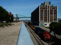 The Pointe St-Charles Switcher is passing an observation deck that gives a good view of the western end of the Port of Montreal as it doubles its train together. At right is a cold storage warehouse that has been converted to condos.