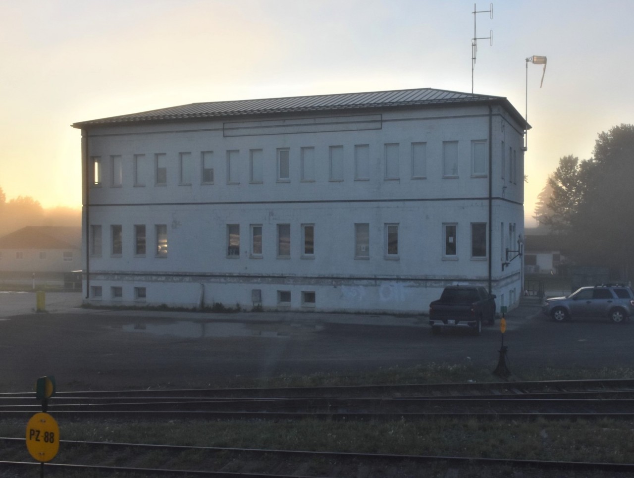 The Hudson Bay Railway headquarters building located at 728 Bignell Avenue in The Pas, MB as seen through my bedroom window in VIA 8202 Chateau Bienville is haloed by the 06:30 morning sun on this cool, foggy August 1, 2022 morning. VIA 693 on its way from Winnipeg to Churchill is rolling into The Pas 4 1/2 hours late but will stand idle long enough for me to detrain and snap a few photos. Had the train been on time (arrive 01:45, depart 02:30) this and other photos at The Pas would have been impossible.