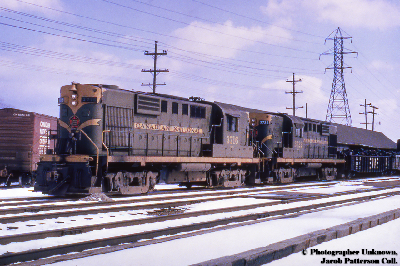 A pair of green and gold MLW RS18s on a westbound freight pause to work the freight shed/fruit platform track at Grimsby, seen beyond the power.  Note the boxcar at left which appears to be on the lead to Grimsby Flour & Feed.  CNR 3716 would later go to the Cape Breton & Central Nova Scotia Railway.  The train slowing on approach to the station can be seen here.A 1953 track layout of Grimsby can be found hereOriginal Photographer Unknown, Jacob Patterson Collection Slide.
