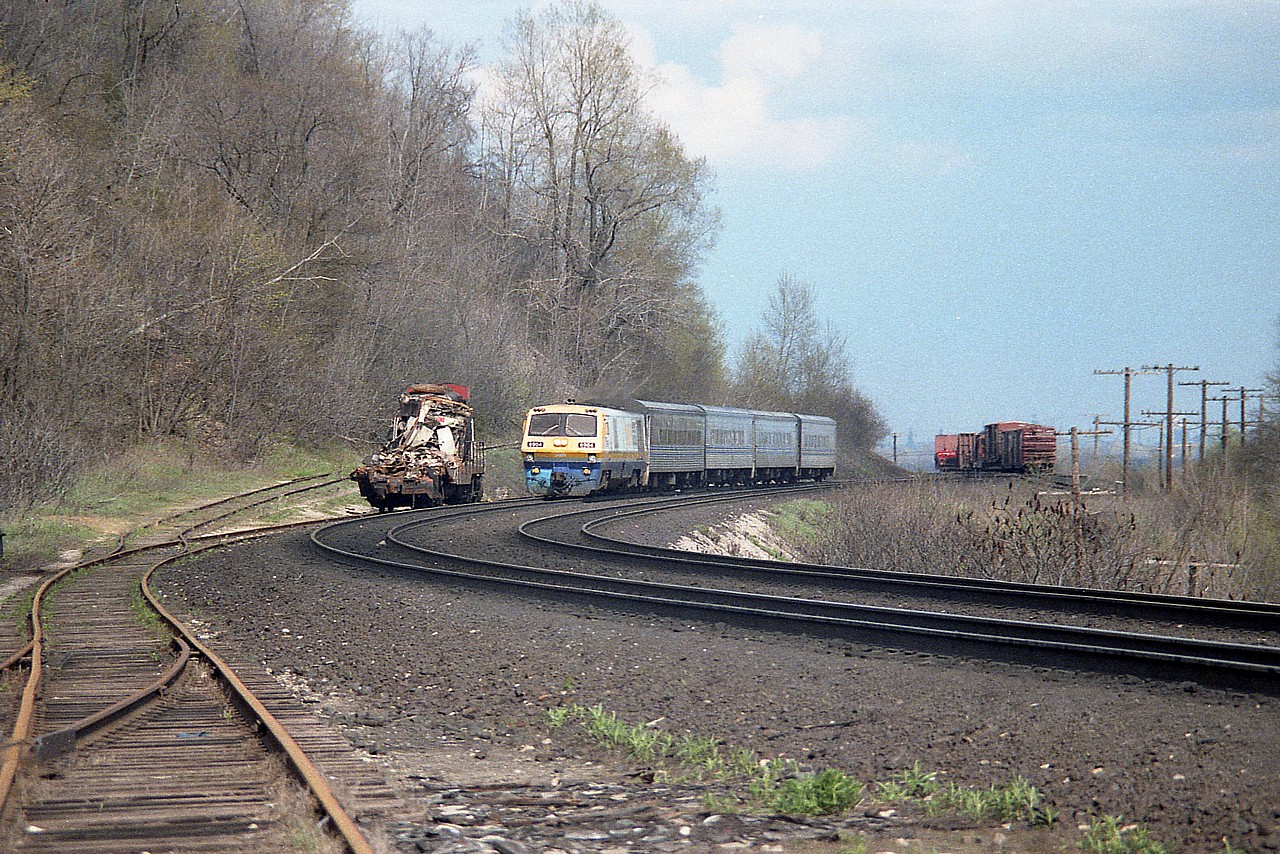BBD LRC-2 #6914 is seen westbound rounding the curve to where old Dundas station was located. Off to the left is wrecked CN GP9 4513, involved in a collision down by mile 2 a few days prior. On the right on the background siding  are rolling stock also involved in the incident.
This scene is of interest since the track shown is now all gone. The foreground track was part of a small yard behind the station and up the grade is the track to the Canada Crushed Stone facility. Out of sight on the right near the rolling stock a track went off down to the lower level where the Steetley (dolomite) plant was located. This track was taken up two years later.
Needless to say, the LRC is history as well. A few have been saved but the units were not reliable, and their life on VIA did not exceed 20 years.