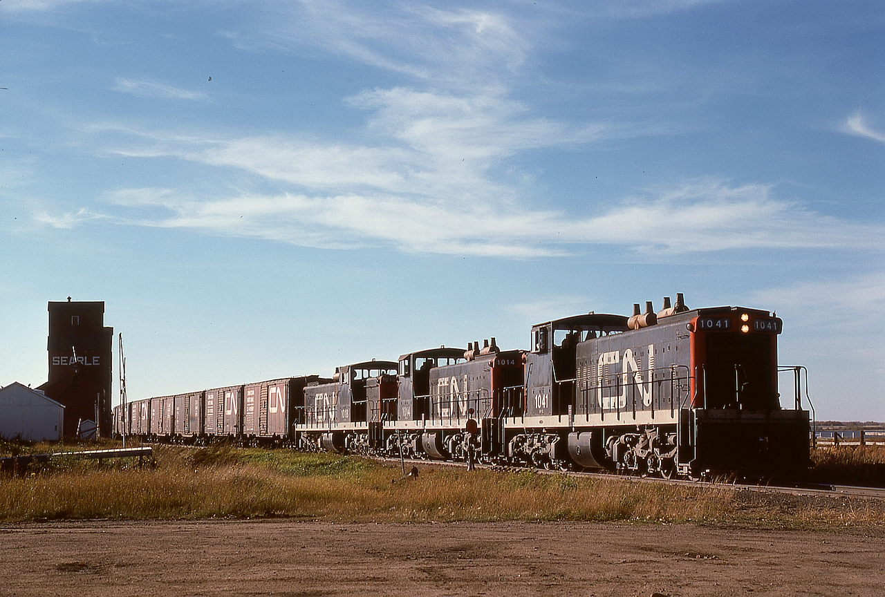 A network of light-rail branchlines radiated from Prince Albert, and on CN that meant GMD-1 power, amply illustrated here with 1041 + 1014 + 1018 on Work Extra 1018 busy lifting loads eastward from the elevators at Spiritwood on Monday 1976-09-27.