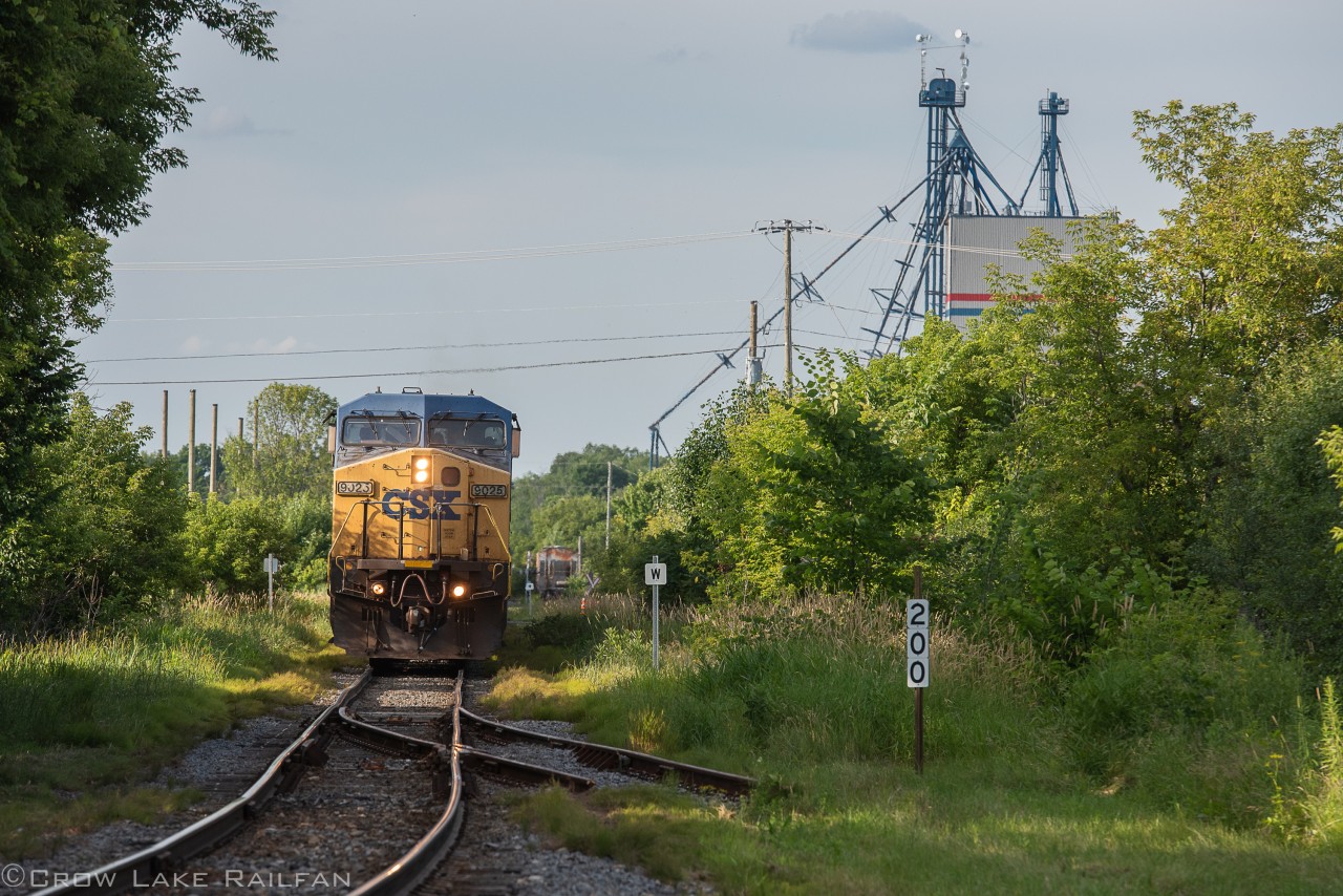 A well worn CSX dash 9W leads CN 327 to the border at Godmanchester, Quebec earlier in the summer. Passing mile 200 of the Montreal Sub and the switch for the wye that has been severed.