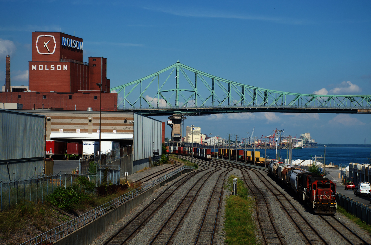 The Pointe St-Charles Switcher is leaving the Port of Montreal with a short train. In the background is the Jacques-Cartier bridge.