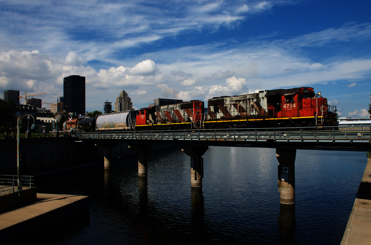 CN 4724's previous paint scheme is visible as a CN noodle starts to show underneath some faded zebra stripes. CN 4787 is trailing as the train exits the Port of Montreal.