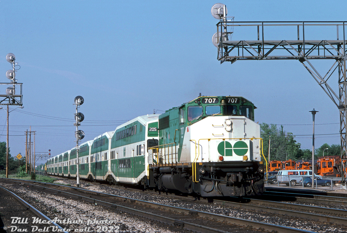 GO Transit GP40-2W 707 leads a 10-car train of bilevel commuter cars through Burlington West bound for Hamilton, after making its station stop at the nearby Burlington GO station. Cab car 205 trails the lead unit, and a 900-series APCU brings up the rear. The two tracks on the left are for CN's Halton Sub mainlines, branching off from the Oakville Sub here.

The old station (hidden by the train) was still in use by VIA at the time, but VIA would soon move its operations to the nearby GO station in another two years. Orange CN maintenance of way equipment sits stored on the Burlington West back tracks.

Bill McArthur photo, Dan Dell'Unto collection slide.