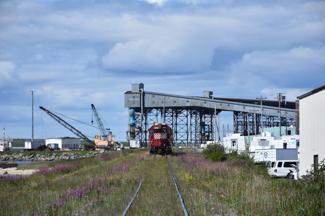 Exhaust gases from the trio of HBR yard switchers blur the steel framework of the Churchill grain elevator conveyor towers as they continue to sort the consist from this mornings wayfreight arrival. A tugboat and a couple of American crawler cranes on a barge sit at the left of the photo, while vehicles and equipment from The Official Tundra Buggy Company fill the maintenance yard on the right. Photos don't seem to convey just how huge this grain elevator complex is.