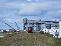 Exhaust gases from the trio of HBR yard switchers blur the steel framework of the Churchill grain elevator conveyor towers as they continue to sort the consist from this mornings wayfreight arrival. A tugboat and a couple of American crawler cranes on a barge sit at the left of the photo, while vehicles and equipment from The Official Tundra Buggy Company fill the maintenance yard on the right. Photos don't seem to convey just how huge this grain elevator complex is.