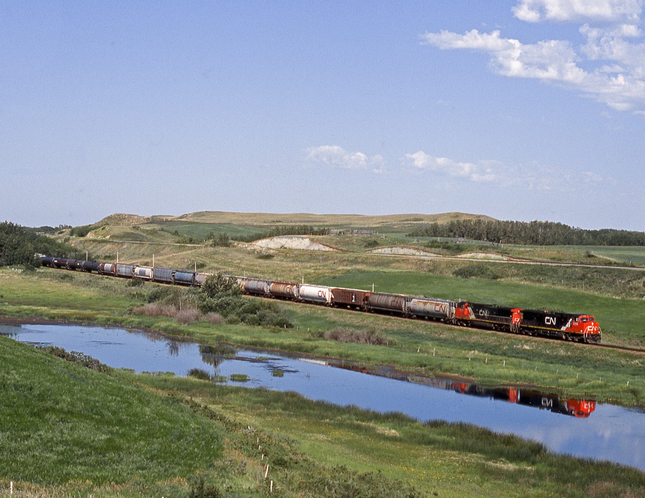 An eastbound just out of the terminal at Biggar rolls through a coulee with the CP,s north main Wilkie Sub. on the ridge above