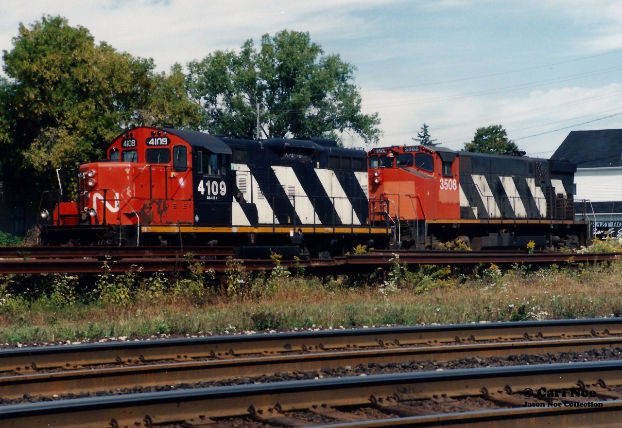 A RaiLink Southern Ontario Railway (RLK) power set is seen laying over in Paris, Ontario with CN 4109 and RLK 3508 with the CN Dundas Subdivision in the foreground.

CN GP9RM 4109 was likely leased at the time. The track the units are sitting on is the CN Dumfries Spur, which went to the Wabco Plant that had closed during the 1970’s. This track at one time crossed Market Street. CN 4109 was eventually retired and is now CBFX 900, while RLK 3508 was sold to the Hudson Bay Railroad and ultimately scrapped.
