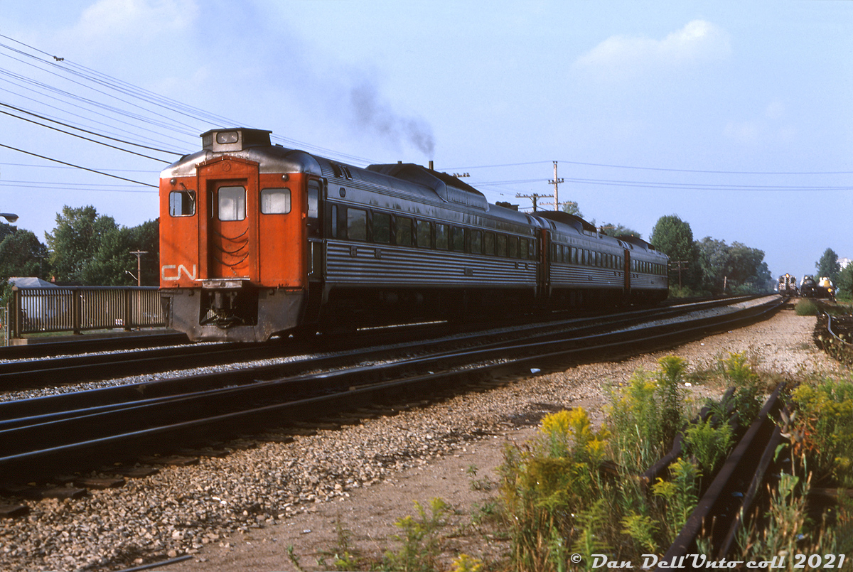 A trio of CN "Railiner" Budd RDC's with RDC-1 6114 trailing accelerate through Port Credit station, eastbound on the Oakville Sub crossing over the Hurontario Street underpass heading eastbound bound for Toronto. 

A CP local freight is visible in the distance switching nearby, utilizing
interswitching rights over the CN Oakville Sub (that CP had running rights over to Hamilton Junction).

As well as the triple track mainline, there were a few service tracks, siding, storage and team tracks here at Port Credit. A spur branched off south (out of view) to the old St. Lawrence Starch plant in Port Credit (demolished in the mid-90's).

Just visivle on the left was the old "shed track" that used to run behind the old CN Port Credit station to the freight shed beside it. The station was demolished sometime around 1973-75 (fell out of favour due to new GO facilities maybe?) and this became a team track.

Original photographer unknown, Dan Dell'Unto collection slide.