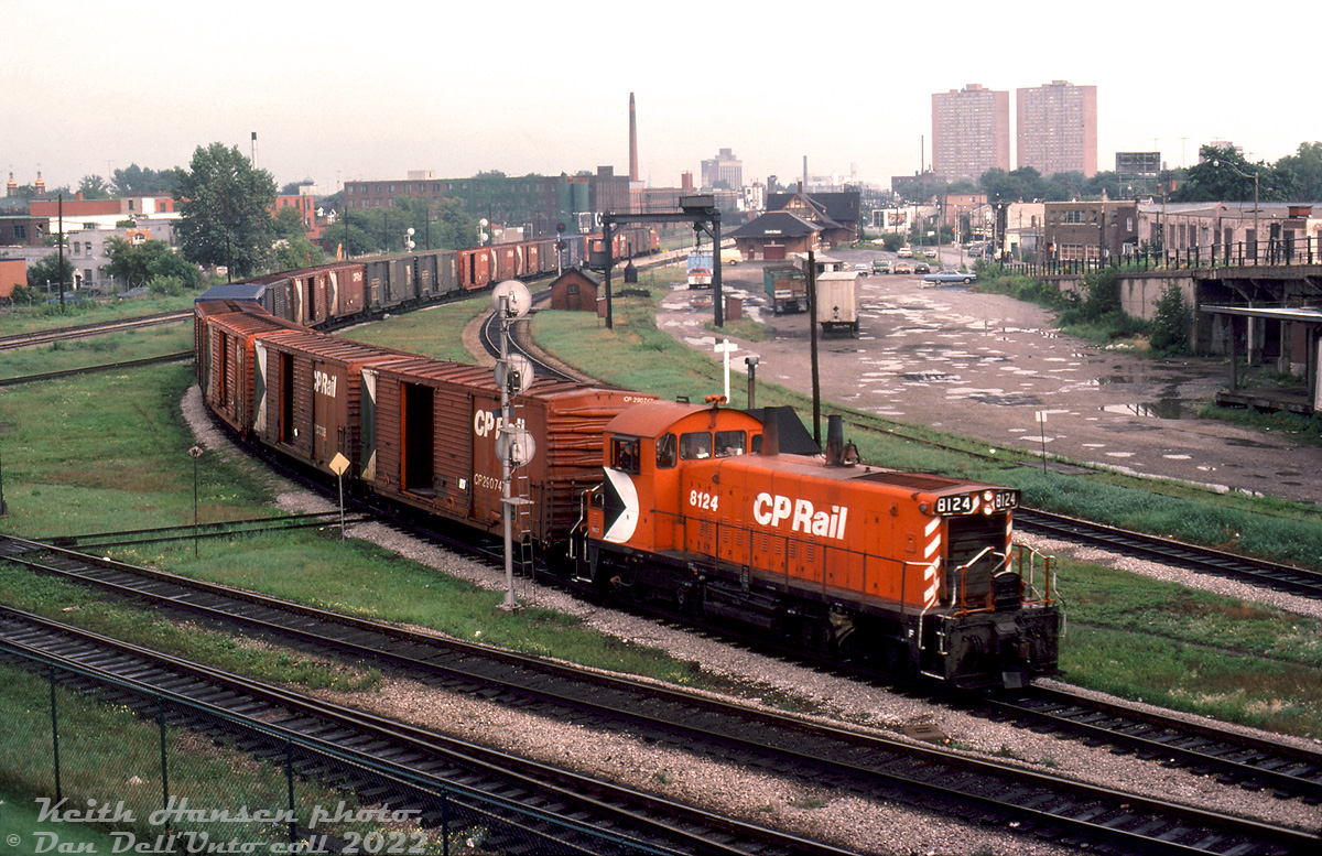 On what appears to be a humid August day, CP SW1200RS 8124 passes through West Toronto with a short local or transfer freight, curving around the southwestern quadrant of West Toronto on the Galt Subdivision after coming north from the Parkdale area, and heading west towards West Toronto/Lambton Yards. This was taken looking south from the old vantage point of Old Weston Road overpass (partially visible on the right), that was closed off to traffic and eventually demolished during the 1980's. It was long a popular train-watching spot dating back to the steam era.

Most of the train appears to be double door 40' boxcars (popular for lumber use), as well as a pair of PGE 50' combo-door boxcars. A wooden van brings up the rear past the platforms of West Toronto Station (demolished in the early 80's by CP while the City of Toronto was trying to have it designated with heritage protection status). The old parking lot and crane track are visible north of the station. In the background, notable buildings include Penfound Varnish (mural obscured by trees to the left), Viceroy Rubber at Dupont (middle), Tower Automotive (lone office tower in the middle background), and The Crossways Mall apartment towers (right). Some of this scene has remained the same, but much has changed dramatically.

Keith Hansen photo, Dan Dell'Unto collection slide.