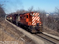 In the 1980's, the TH&B's motive power situation was getting dire due to reliability issues with its small fleet of aging first generation diesels. Parent CP Rail was often lending 4-axle power including RS18, C424, and leased B&O GP38 units. Here, CP RS18's 8733 and 8791 lead TH&B GP9 401, NW2 51 and SW9 57 in a mix of 251 and 567 noise as they climb "the mountain" out of Hamilton with a heavy rock train, seen here at Dewitt Road on the ascent to Vinemount. The two switchers were some of the only ones in the fleet equipped with MU, so were often seen working mainline trains with TH&B's Geeps and leased CP power. In a few more years, motive power officials with CP would retire the TH&B's fleet of switchers, and have the Geeps (most ended up stored <a href=http://www.railpictures.ca/?attachment_id=1564><b>out of service at John Street</b></a> upon major failure) rebuilt as fresh <a href=http://www.railpictures.ca/?attachment_id=46873><b>CP 1680-series GP7u</b></a> and GP9u yard units.
<br><br>
<i>Reg Button photo, Dan Dell'Unto collection slide.</i>