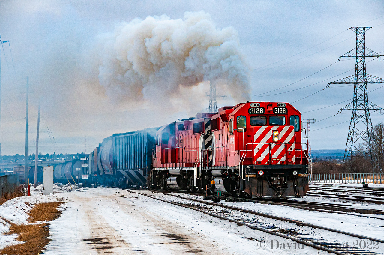 "Throttle Eight, don't be late! The engineer of this Thunder Bay yard job has unleashed all the horses of his two GP38-2's as the CP 3128 and CP 3029 struggle to lift a track of grain loads at "the Pocket", creating this spectacular scene, covering the intercity area in a cloud of diesel exhaust.