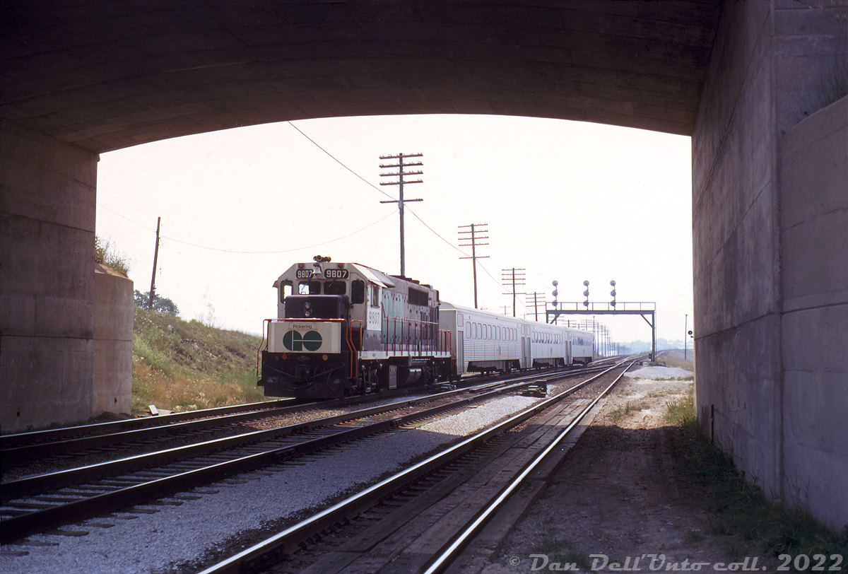 Ducking under Liverpool Road overpass, GO Transit GP40TC 9807 trails a westbound 3-car consist of Hawkers (with cab car 9855 leading) that has just departed Pickering GO Station, and is heading through the plant at "Liverpool" on CN's Kingston Subdivision.

As GO was still in its infancy, Pickering was the easternmost station on its initial Oakville-Pickering Lakeshore corridor, and the GO Sub didn't exist yet. The track branching off to the right on the incline is CN's York Sub, part of the "Toronto Bypass" project that helped divert CN freight traffic around Toronto and made a new GO commuter service possible.

Original photographer unknown, Dan Dell'Unto collection slide.