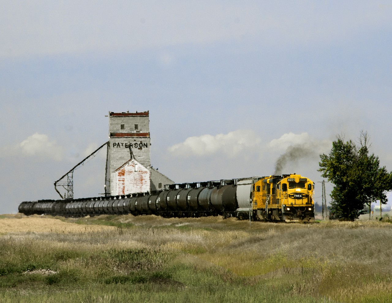 Great Sandhills eastbound from Home terminal of Leader to Swift Current with leased NREX power still with Santa Fe Colours passes the wooden elevator at Prelate on The former CP secondary line from Swift Current to Bassano. The tank cars are a combo of LPG loads from the Empress gas Plant near Burstall and the empties out of storage