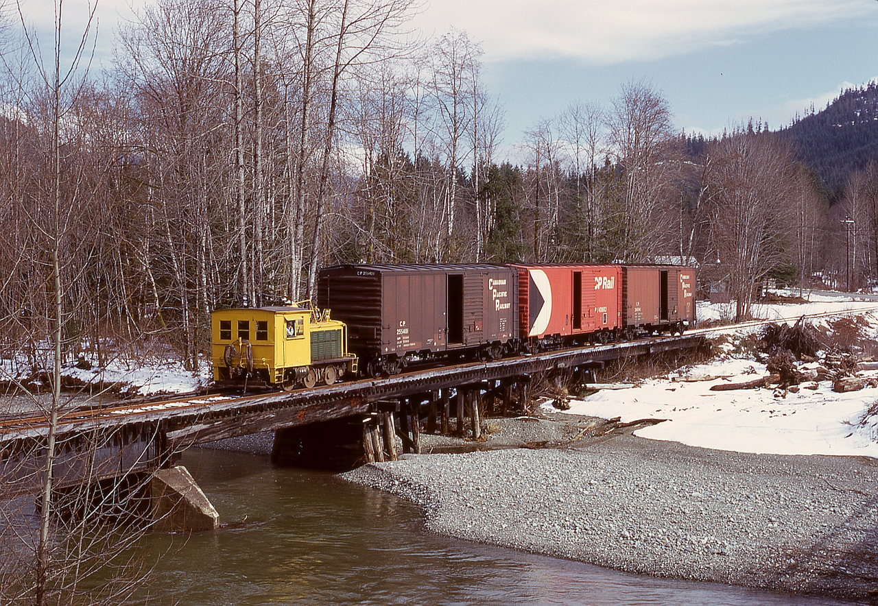 On Vancouver Island, and between the Lake Cowichan interchange with the E&N and their mill at Honeymoon Bay, Western Forest Industries operated a 1929 Plymouth WLG-8 locomotive numbered 40 (previously 7) as required to bring empties to the mill and take resulting outbound loads to the interchange for furtherance to off-Island destinations.  Here, WFI 40 has three empties in tow and is crossing the Robertson River bridge westward on a cool Monday 1974-03 -11, with less than two miles to go to reach the mill.

Number 40 went to Westcan Terminals at Ogden Point in Victoria in 1978, where it regained its number 7, then went to the Ladysmith museum in 1987 and then in 1996 to the Kaatza Museum in Lake Cowichan in 1996, where it is now on display, just 6 km (as the raven flies) east-northeast of this photo location.