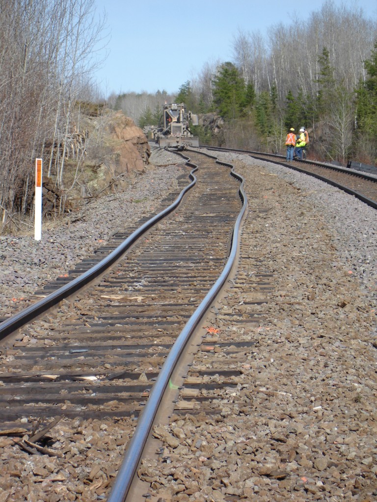 Warm & wobbly. It's April 20, 2010 and springtime near Minaki, ON in northwestern Ontario, but it's a hot day on the track. The combination of full sun, disturbed ballast, changing of track ties, and the movement of machinery over warm rails has resulted in a series of sun kinks through this curve on CN's Redditt Sub. It was quite the feeling when the rail began to 'snake' under the wheels of the ballast regulator I was in as it rounded the curve in this picturesque rock cut area. Even as I was taking photographs of the initial kinks the rail continued to flex in additional locations. It wouldn't be long before the regulator and a production tamper teamed up to methodically get the track section back to where it was supposed to be. Just another day on the track with a production tie gang. :-)
