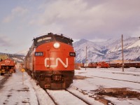 CN #1 The Super Continental has arrived in Jasper, AB on this frigid November day and is in the process of being fully serviced during this multi-hour station stop. New head-end crew, fuel, water, ice, and everything else that came with a division point stop back in the mid-1970's. From left to right in this photo there is so much to see. The CN Jasper station, a CN supply truck, a CN fuel truck and driver, baggage tug and attendant, CN 6513 GMD FP9A, vans, snowplows, white fleet units, Jasper Auxiliary cars, the CN roundhouse, and the mountains. One rule back then ... “Kindly flush toilet after each use except when train is standing in station.”