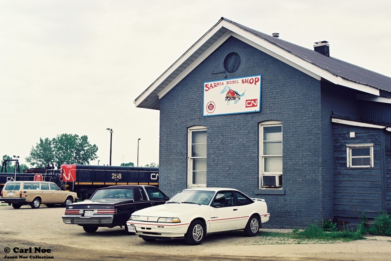 A portion of the CN Sarnia, Ontario diesel shop is viewed during a hazy summer day with GP9 Slugs and SW1200RS’s waiting for their next assignments.