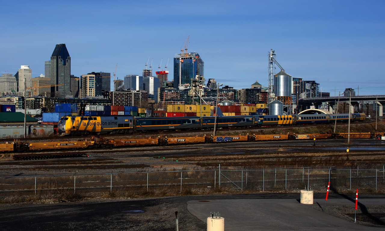 VIA 65 with VIA 909 and six LRC cars pass some well cars that will be heading to the Port of Montreal.