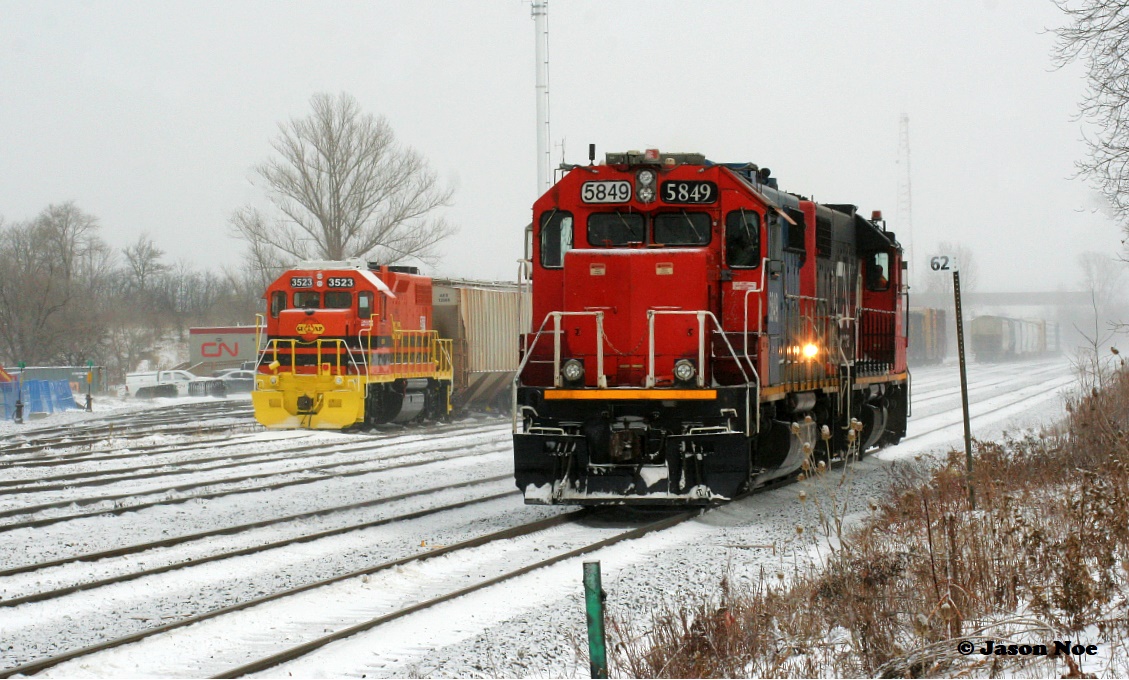 CN L540 with GTW 5849 and CN 7515 slowly cruise down the Guelph Subdivision passing the Kitchener yard with Goderich-Exeter Railway’s newest unit, GEXR GP38-2 3523 looking on during a winter storm. L540 would eventually reverse into the yard, as the crew would be ready to end their shift ahead of Christmas.